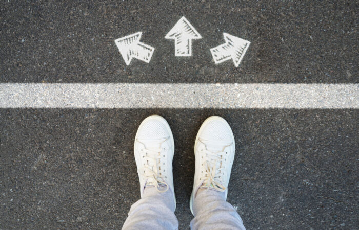 Symbolbild Richtungsentscheidung Mann steht auf einer Straße mit aufgemalten Richtungspfeilen